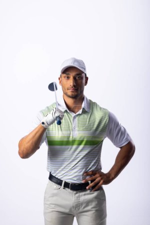 Young biracial man poses confidently with a golf club. His attire and equipment suggest he is a skilled golfer ready for a game.