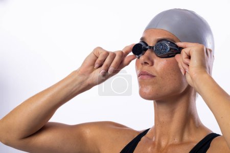 Junge kaukasische Schwimmerin passt ihre Schwimmbrille an. Sie bereitet sich auf das Schwimmen vor, zeigt athletische Bereitschaft und Konzentration.