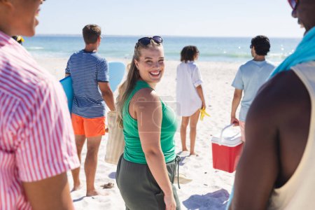 Young Caucasian woman enjoys a sunny beach day with friends. Group of diverse individuals gather for a relaxing outdoor event by the sea.