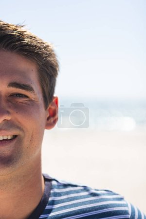 A young Caucasian man smiles at the beach, with copy space. His relaxed demeanor suggests a leisurely day outdoors by the sea, unaltered.