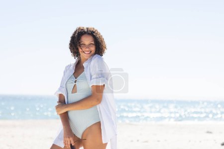 Young biracial woman enjoys a sunny beach day. She radiates happiness while relaxing by the sea, unaltered, with copy space.