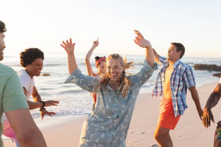 Freunde genießen eine ausgelassene Strandparty bei Sonnenuntergang. Die Lach- und Tanzbewegungen der Gruppe schaffen eine lebendige Atmosphäre im Freien.