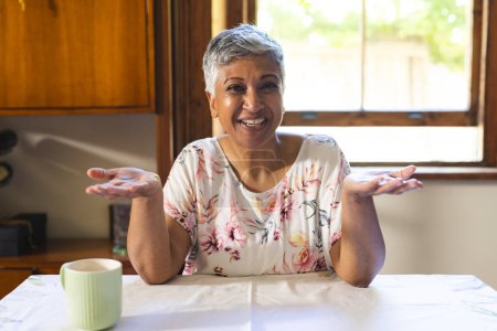 Una mujer madura birracial sonríe calurosamente en casa en una videollamada. Ella emana un ambiente acogedor, inalterado, en un ambiente acogedor cocina.