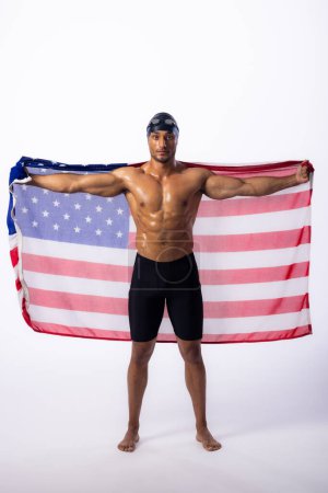 Biracial male athlete displaying the American flag, with copy space. Pride and patriotism shine as the swimmer showcases national colors in a studio setting.