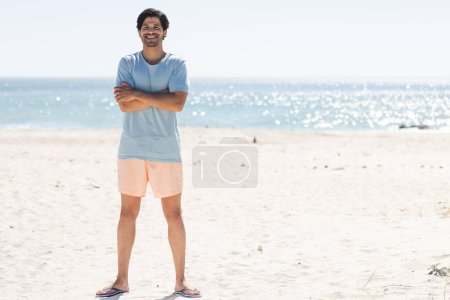 Selbstbewusst steht der junge Mann an einem sonnigen Strand mit Kopierraum. Seine lässige Kleidung lässt auf einen entspannten Tag am Meer schließen..