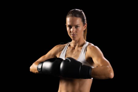Jeune femme caucasienne pose avec confiance dans le matériel de boxe, avec de l'espace de copie. Son expression ciblée et sa construction athlétique soulignent son dévouement envers le sport.