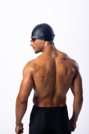 Die athletische, zweirassige männliche Schwimmerin posiert selbstbewusst. Seine Badekappe und seine Brille deuten auf die Vorbereitung auf ein Wettschwimmen hin..