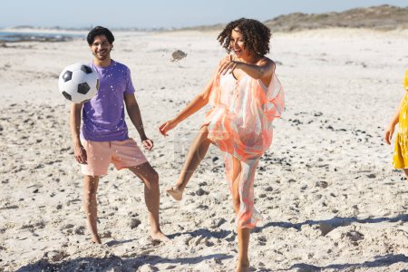 Young biracial couple enjoys a soccer game on the beach. Their laughter and soccer game add a vibrant energy to the sunny outdoor setting.