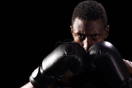 African American man in boxing gloves focuses intently. His determination is evident as he prepares for a match or training session.