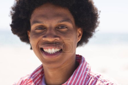 A young African American man smiles brightly at the beach. Outdoor setting enhances the cheerful vibe of the portrait unaltered.