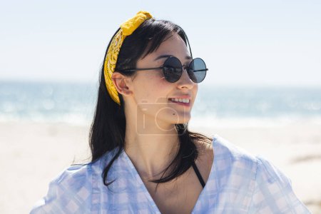 Junge Frau genießt einen sonnigen Strandtag. Ihr entspanntes Auftreten und ihre stylische Sonnenbrille beschwören unverändert ein Gefühl sommerlicher Freizeit herauf..