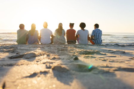 Diverse Freunde sitzen am Strand, mit Kopierraum. Gemeinsam genießen sie einen ruhigen Sonnenuntergang und schaffen bleibende Erinnerungen im Freien.