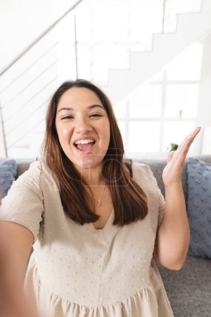 Young biracial woman smiles warmly in a bright home setting on a video call. Her cheerful expression invites a sense of welcome and friendliness.
