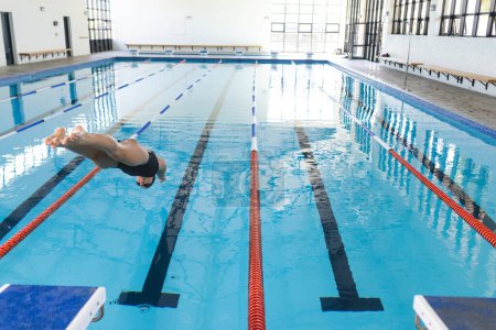 Athlete dives into an indoor swimming pool.  The image captures the dynamic start of a swimmer's training session.