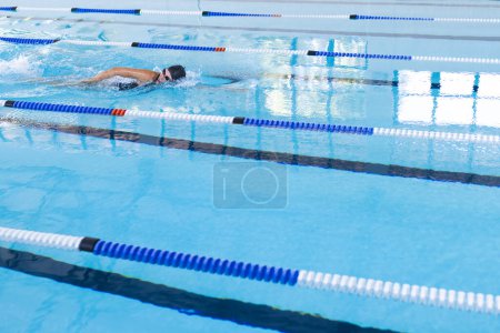 A swimmer practices in a pool, with copy space. The clear blue water indicates a clean and well-maintained indoor swimming facility.