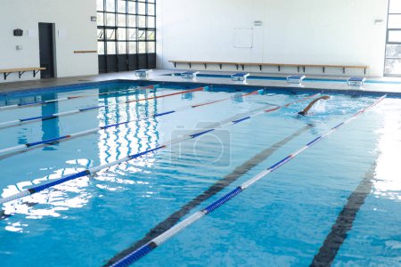 Ein Schwimmer übt in einem Hallenbad auf einer Sportanlage. Die Bahnen sind für Wettkampftraining oder Freizeitschwimmen klar gekennzeichnet.