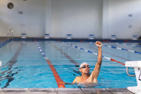 A swimmer reaches the end of the pool in an indoor facility.  The athlete's determination is evident in this competitive swimming environment. 