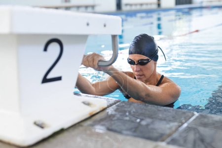 Die kaukasische Athletenschwimmerin bereitet sich auf das Schwimmen im Hallenbad vor. Ihr konzentrierter Ausdruck fängt die Intensität des Wettkampfschwimmens ein.
