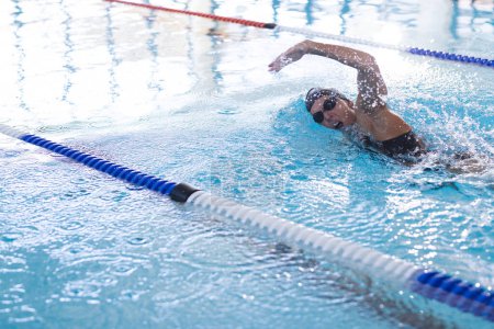 Caucasian female athlete swimmer swims in an indoor pool.  She's practicing her freestyle stroke in a competitive swimming environment.