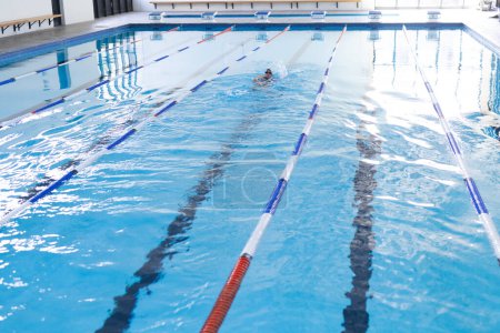 La personne pratique la natation dans une piscine intérieure claire, avec espace de copie. Les diviseurs tranquilles de l'eau et de la voie préparent un cadre serein pour l'exercice et l'entraînement.