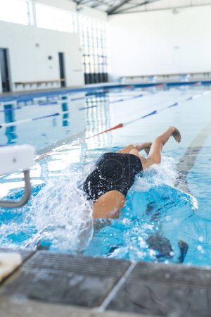 Kaukasische Sportschwimmerin taucht in ein Schwimmbad ein. Zum Zeitpunkt des Eintritts gefangen, übt sie in einem Hallenbad.