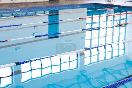 Empty lanes in a serene indoor swimming pool await swimmers. Calm water reflects the tranquility of a facility designed for sport and leisure.