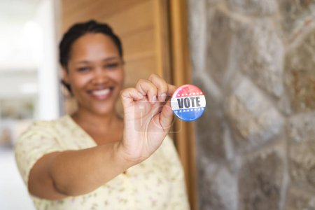 A young biracial woman shows off a 'Vote' badge proudly. Her gesture promotes civic engagement and the importance of voting.