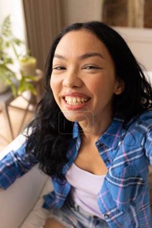 Young biracial woman smiles brightly. Casual attire suggests a relaxed setting at home or a casual gathering.