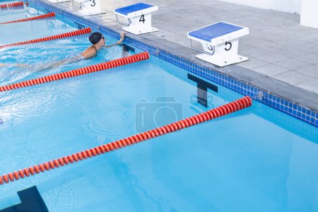 Schwimmer taucht bei Wettkämpfen in ein Becken ein, mit Kopierraum. Das Bild fängt den dynamischen Start eines Rennens in einer Schwimmhalle ein.