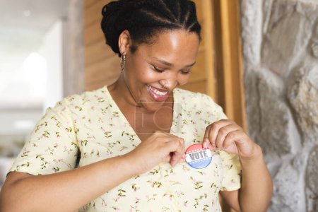 Young biracial woman pins a 'Vote' sticker on her shirt. Captures a moment of civic pride and participation at home.