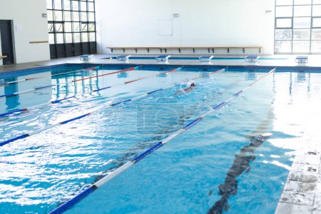 Ein Einzelschwimmer übt in einem Hallenbad mit Kopierraum. Das Setting legt einen Fokus auf Fitness oder Training nahe, in einer Schule oder einem Gemeindezentrum.