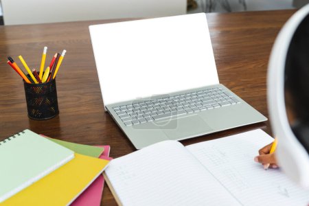 El estudiante se involucra en el aprendizaje en línea en casa, con espacio para copiar. Un portátil con pantalla en blanco es central, lo que sugiere un enfoque en la tecnología de la educación.