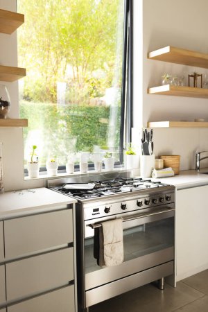 A modern kitchen features a stainless steel stove and white countertops with copy space. Sunlight streams in through the window, highlighting the clean and organized cooking space.
