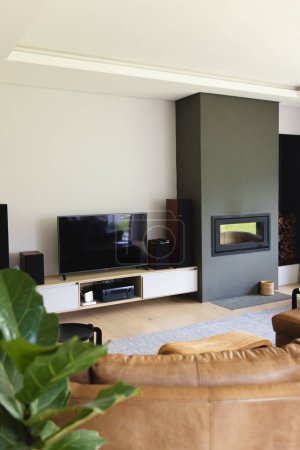 El moderno salón cuenta con TV de pantalla plana, chimenea y sofá de cuero marrón. plantas verdes añaden un toque de naturaleza, mientras que los tonos neutros de la habitación crean un ambiente acogedor.