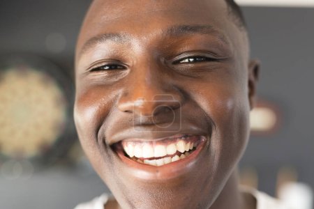 Großaufnahme eines lächelnden jungen afroamerikanischen Mannes mit kurzen schwarzen Haaren. Sein strahlendes Lächeln und die Inneneinrichtung suggerieren einen Moment der Freude und Entspannung.