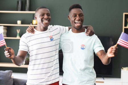 Two young African American men are holding American flags, wearing "I Voted" stickers. Their joyful expressions suggest they are celebrating their participation in the democratic process.