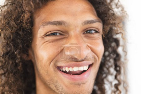 Young biracial man with curly hair smiles brightly. His joyful expression suggests a moment of happiness or amusement.