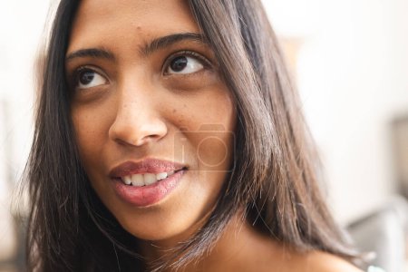 Young biracial woman with brown eyes and shoulder-length hair smiles subtly. Freckles dot her cheeks, and the indoor lighting highlights her features.