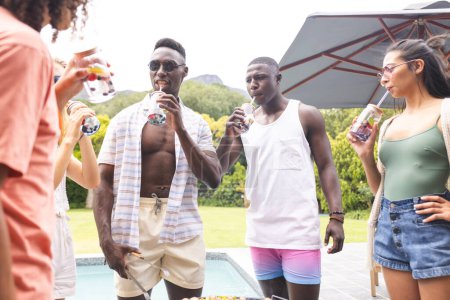 Young African American man sips a drink beside a biracial woman at a pool party. They are enjoying a sunny day outdoors with friends, in a casual, social setting.