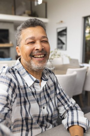 A senior biracial male radiates joy in a home setting. His salt-and-pepper hair complements the laughter lines on his face, unaltered