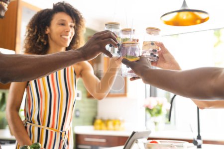 Una pareja diversa brinda con batidos saludables en una cocina soleada. La mujer afroamericana tiene el pelo rizado, y el hombre está en forma con el pelo corto, inalterado