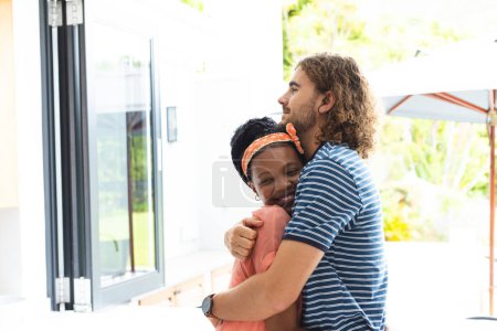A diverse couple embraces warmly, smiling, with copy space at home. The woman is African American with a bright headband, and the man is Caucasian with curly hair, unaltered.