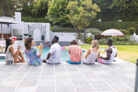 Un grupo diverso de amigos se reúne junto a la piscina con espacio para copiar. El hombre afroamericano habla animadamente, rodeado de sus compañeros con atuendo casual de verano, inalterado.
