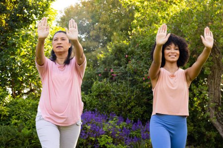 Mature biracial woman and young biracial woman practicing yoga outdoors, at home. Both wearing casual clothes, mother has short black hair, the daughter curly, unaltered