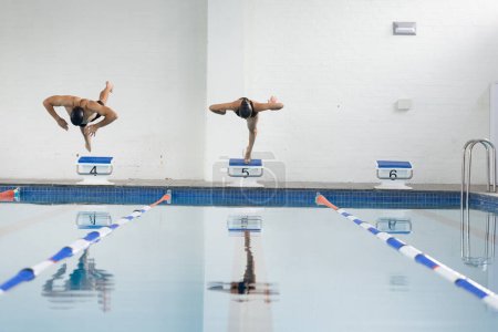 Divers jeunes nageurs plongeant dans la piscine intérieure, espace de copie. Une femme biraciale et un homme caucasien, tous deux athlétiques, aux cheveux foncés et bruns respectivement, jouissant d'eau, inaltérés