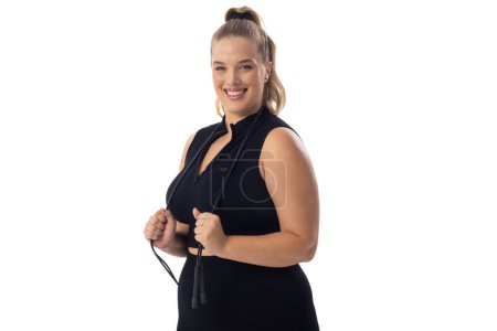 A Caucasian young female plus size model with white background, copy space. She holds a jump rope, wears black, and smiles, embodying body positivity, unaltered
