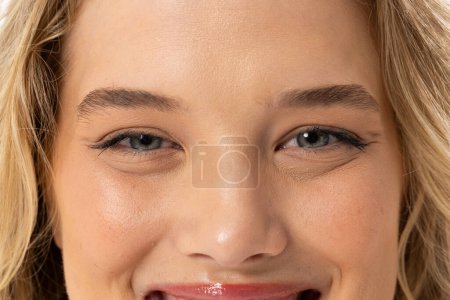 Caucasian young female plus size model with light makeup is smiling on white background, embodying body positivity. She has blonde hair, light skin with freckles, and brown eyes, unaltered.