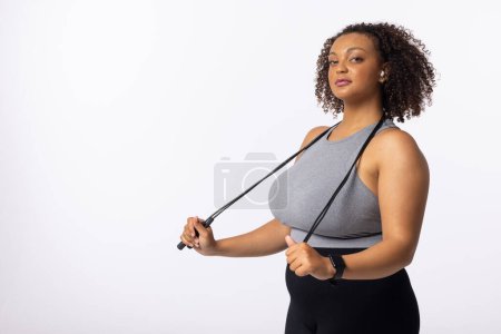 A biracial young female plus size model holds resistance bands on white background, copy space. She has curly brown hair, light brown skin, and promotes body positivity, unaltered