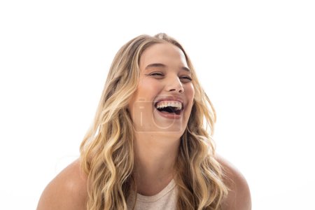 Young Caucasian female plus size model laughing, showing joy on white background, copy space. She has long, wavy blonde hair and clear skin, unaltered, embodying body positivity.