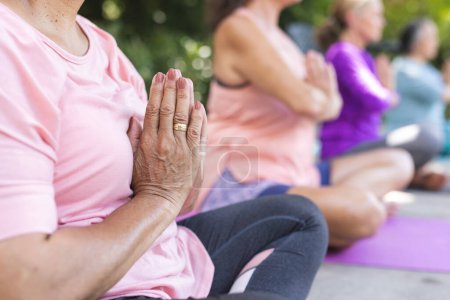 Draußen praktizieren diverse ältere Freundinnen Yoga. Lässige Fitnesskleidung tragen, sich auf Posen konzentrieren, ruhige Momente gemeinsam genießen. 